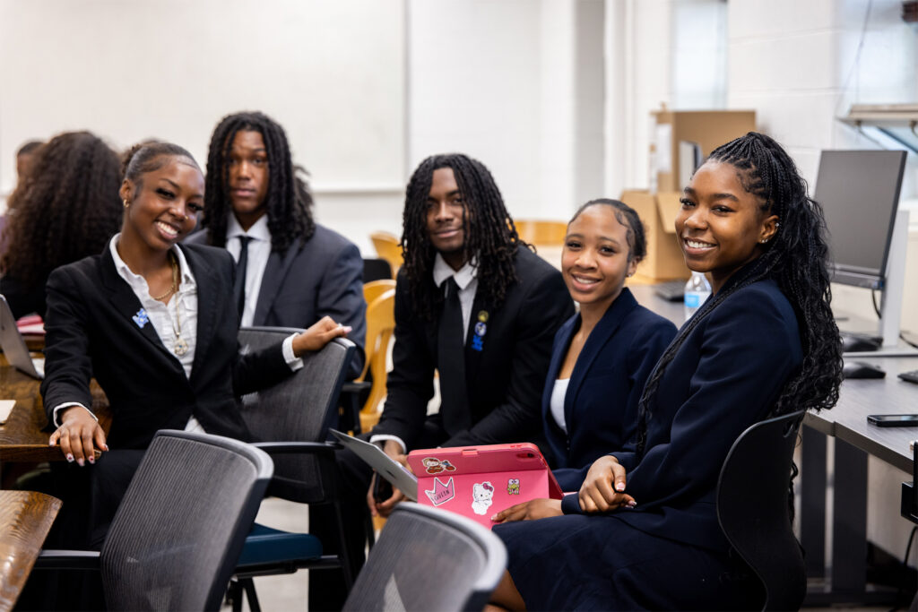 A group of students in business professional attire smiling at the camera.
