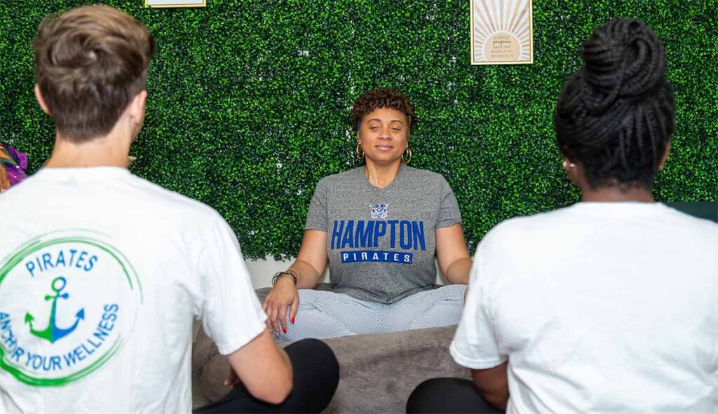 A photo of the Athletics and Band Specialist leading a relaxation session with two students. Behind them is a green ivy covered wall.