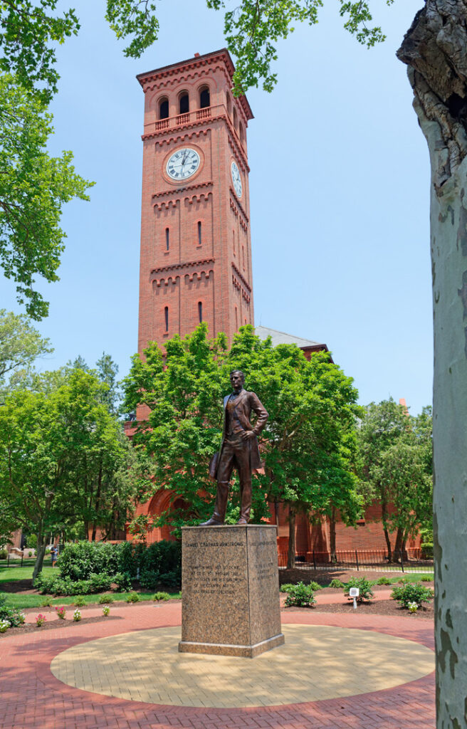 Photo of the Hampton University iconic clocktower. In front of it stands a statue of Samuel Chapman Armstrong.