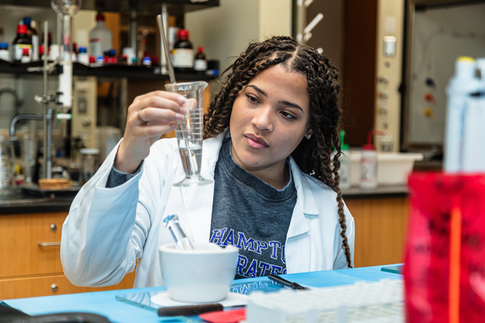 A Pharmacy student holds up to examine a beaker filled with a clear fluid.