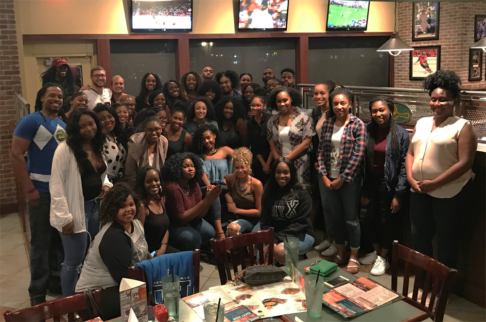 A photo of a large group of students in casual wear posing for the camera at a restaurant.