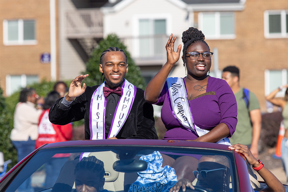 A photo of Mister and Miss Hampton University waving while sitting high-up in a car in the parade.