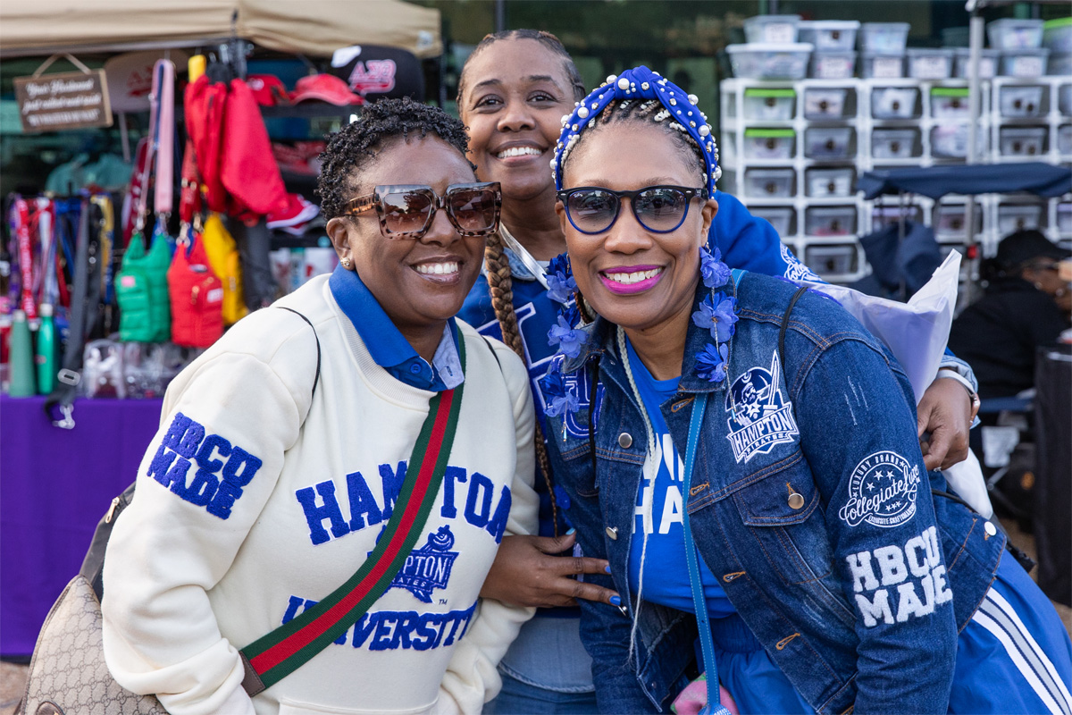 A photo of three alumna posing for the camera with a vendor's booth in the background.