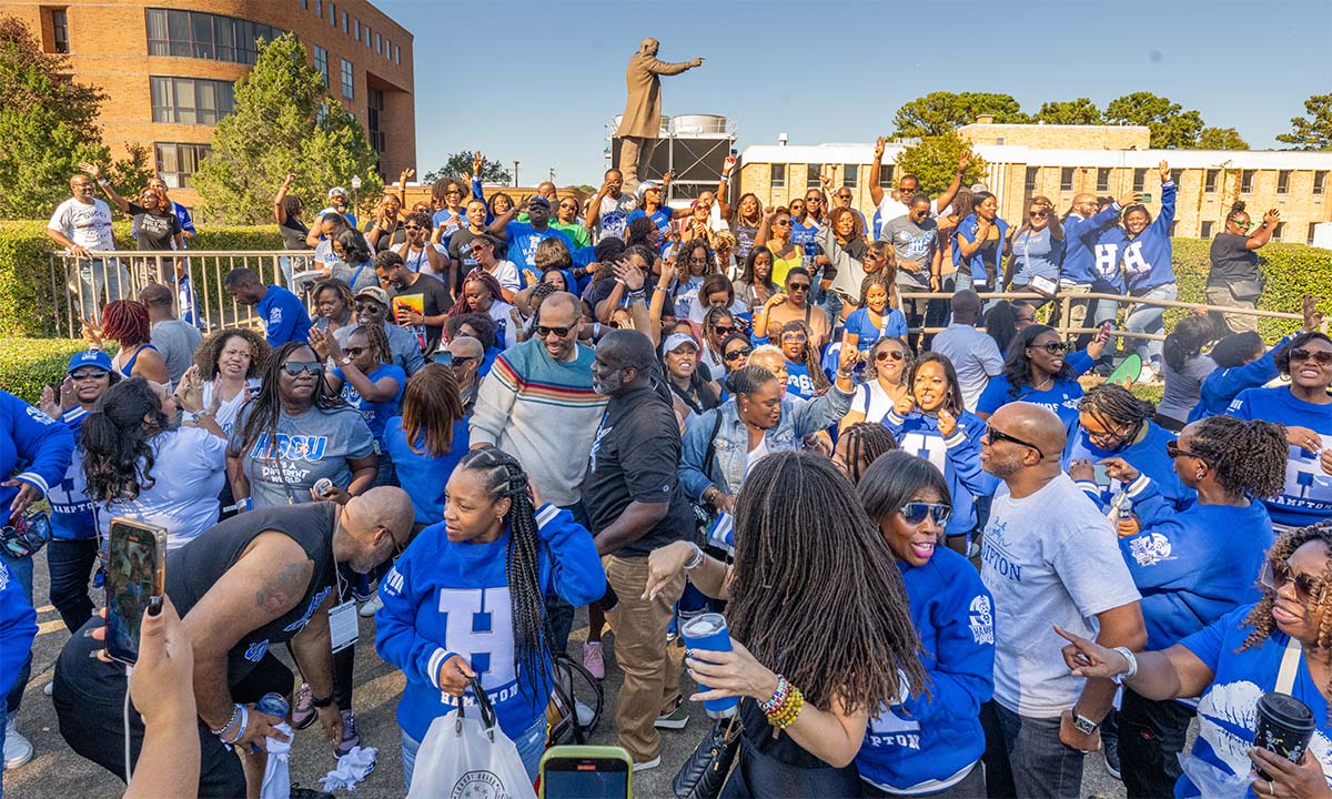 A photo of a large group of alumni posing for the camera in front of the Booker T. Washington memorial statue.