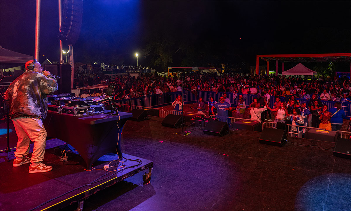 A photo of the alumni crowd at the homecoming 2023 event, The Escape Remixer. A man is singing on stage in the foreground.