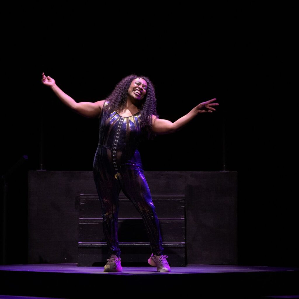 A photo of Tiffany Jackson performing on stage under purple lights.