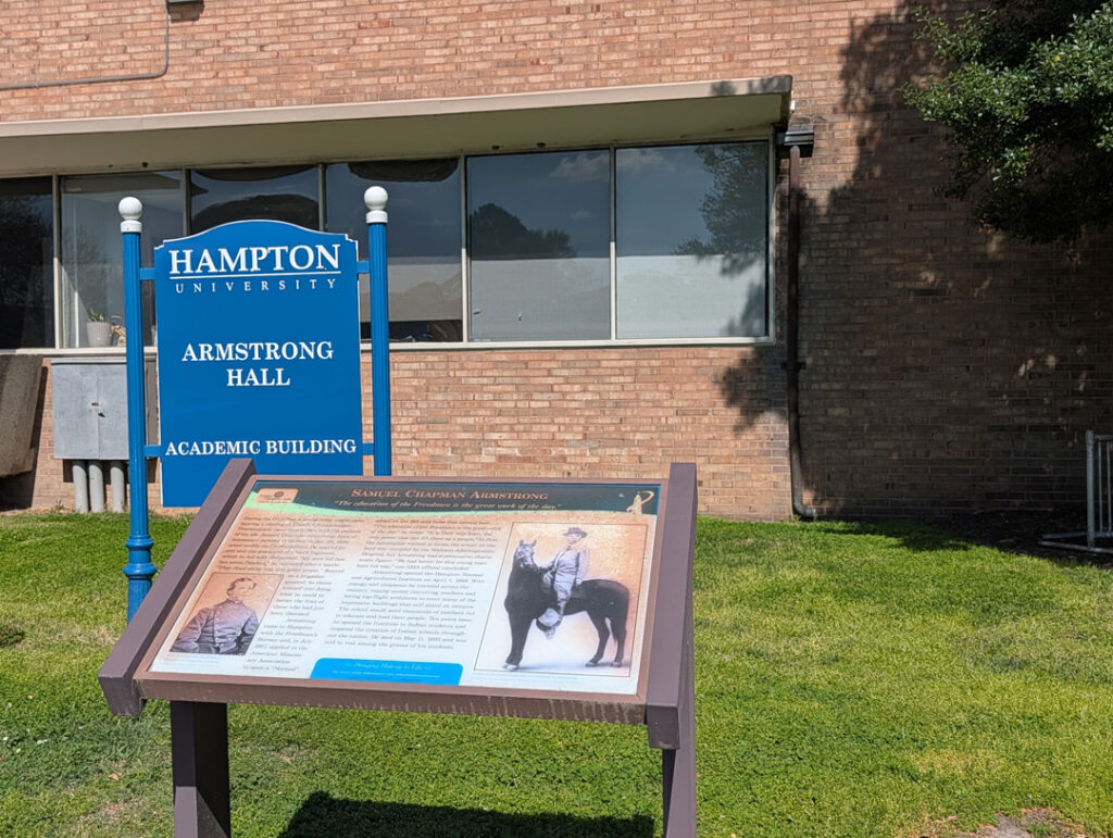A photo of the Armstrong Hall building with a standing plaque describing the namesake of the building.
