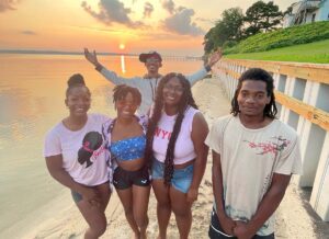 A photo a Bereavement Services Program participants facing the camera and smiling while standing on a beach with the sunsetting behind them. They are wearing beach appropriate outfits.