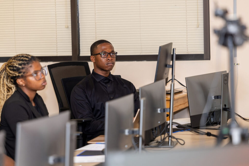 Students sit at computers while listening to a presentation.