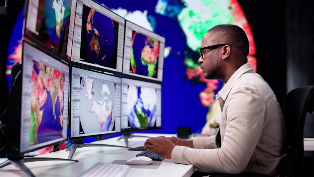 A man looks at a row of computer screens displaying atmospheric data.