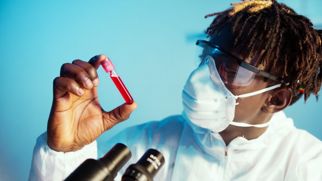 A student wearing a medical mask and goggles looking a testing tube filled with a red liquid.