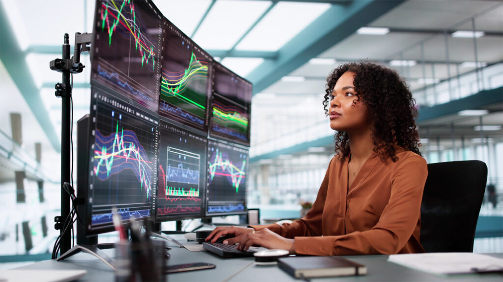 A female student looks at a row of monitors displaying financial analytics.