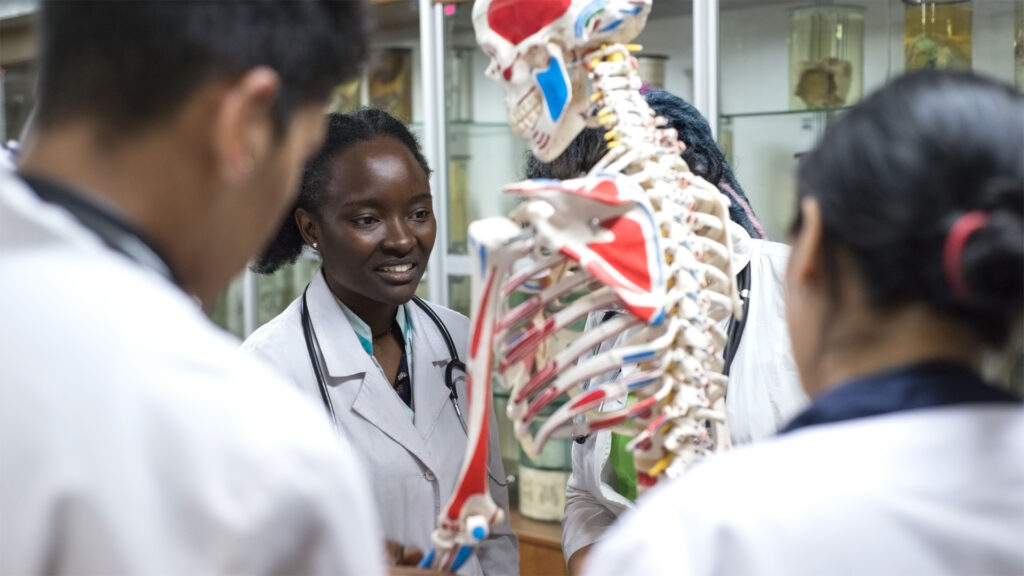 Students wearing white medical examiner coats examine an anatomical model.