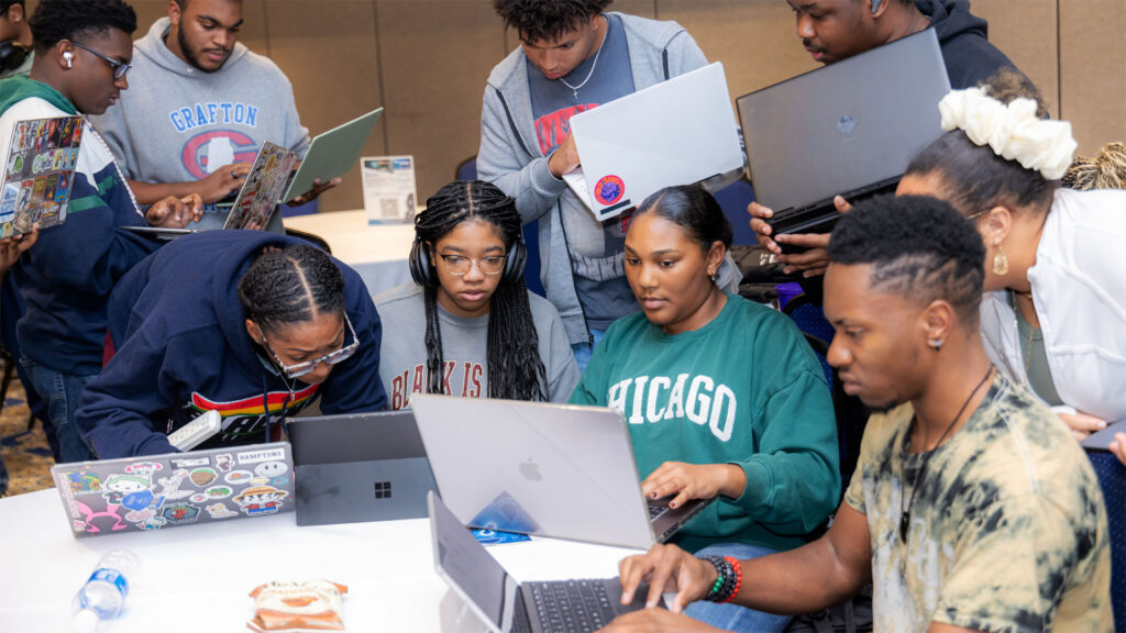 A group of students with laptops discuss a coding project.