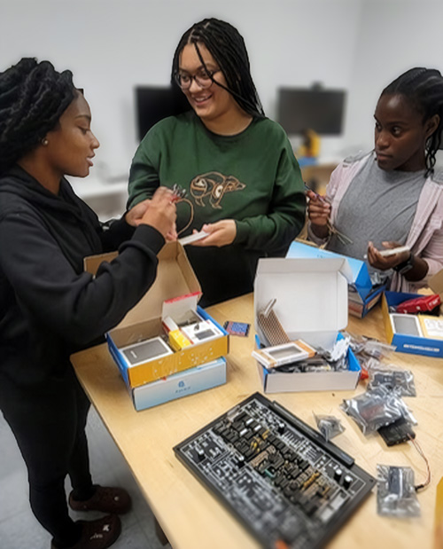Three students examine a printed circuit board kit.