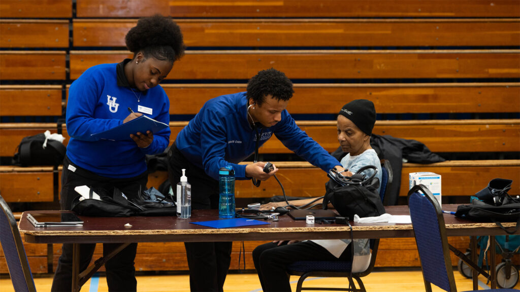 Students assist with a health screening for older woman.