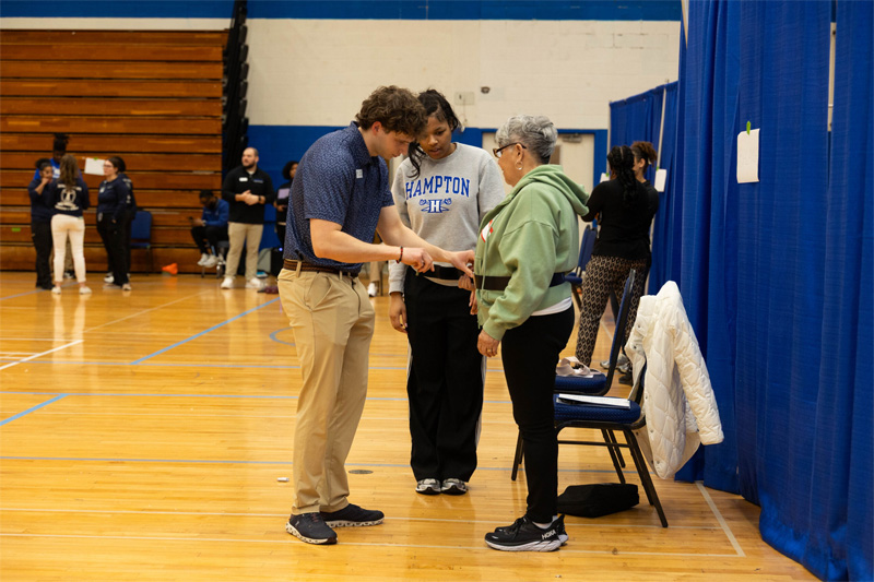 A students assists a senior attendee with a waist measurement.