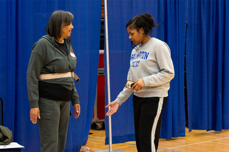 A student demonstrates and talks to a senior attendee about their legs.