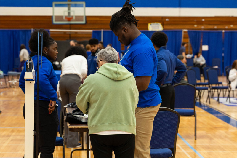 A student clinician prepares to take a height and weight measurement of a senior attendee.