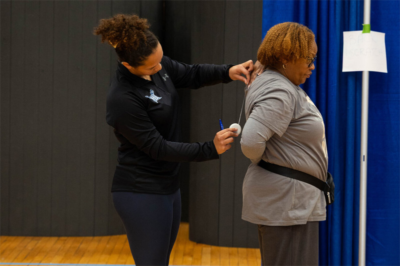 A student clinician take a spinal measurement of a senior attendee.