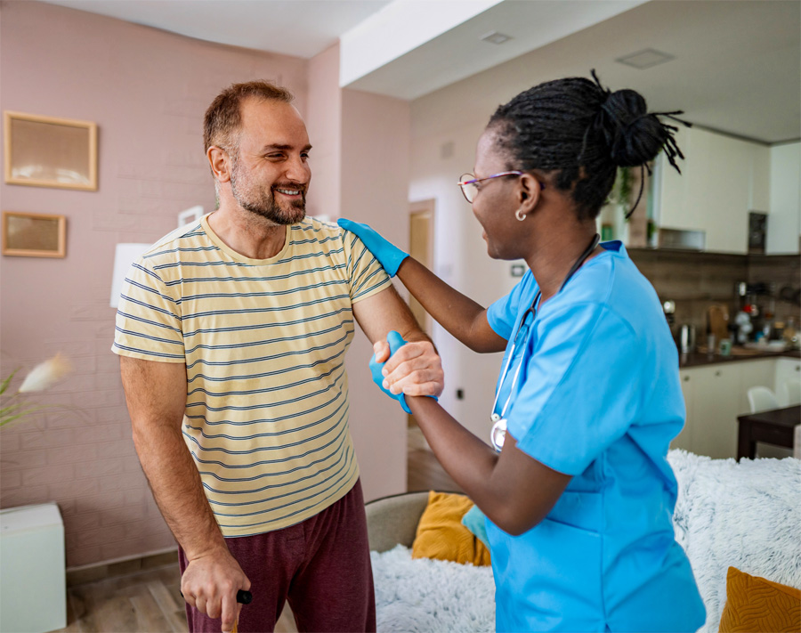 A photo of a health professional helping a patient to steady himself while they both smile at each other.