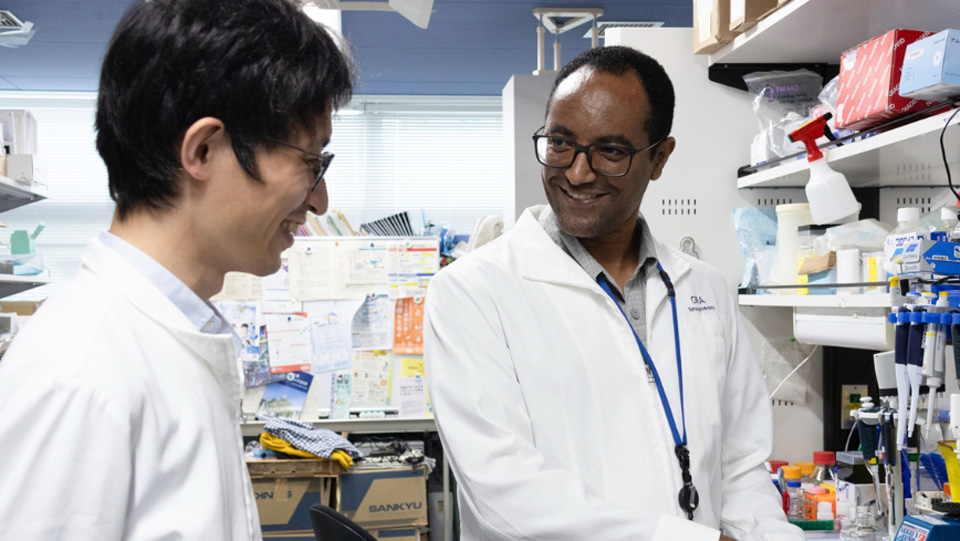 A photo of Mengistu Shukare and a student wearing white lab coats in a lab environment.